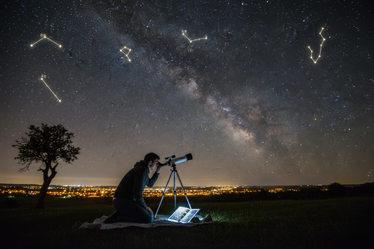 Beginner stargazer using small telescope with star chart under night sky filled with visible constellations